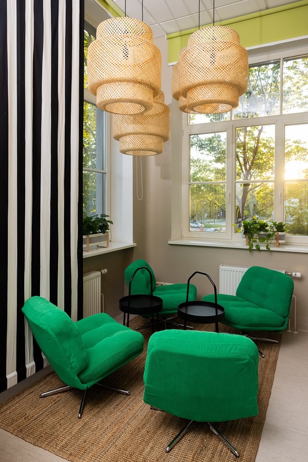 Уютная зона отдыха в офисе с зелёными креслами, чёрными приставными столиками и плетёными подвесными светильниками
