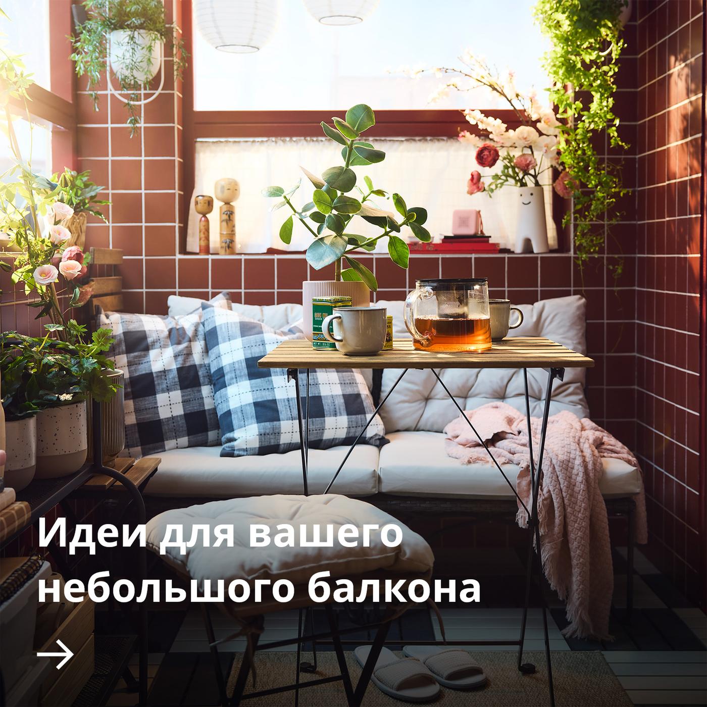 Уютный балкон с красной плиткой, клетчатыми подушками на скамье, небольшим деревянным столиком с кружками и стеклянным чайником, а также растениями в горшках в мягком солнечном свете.