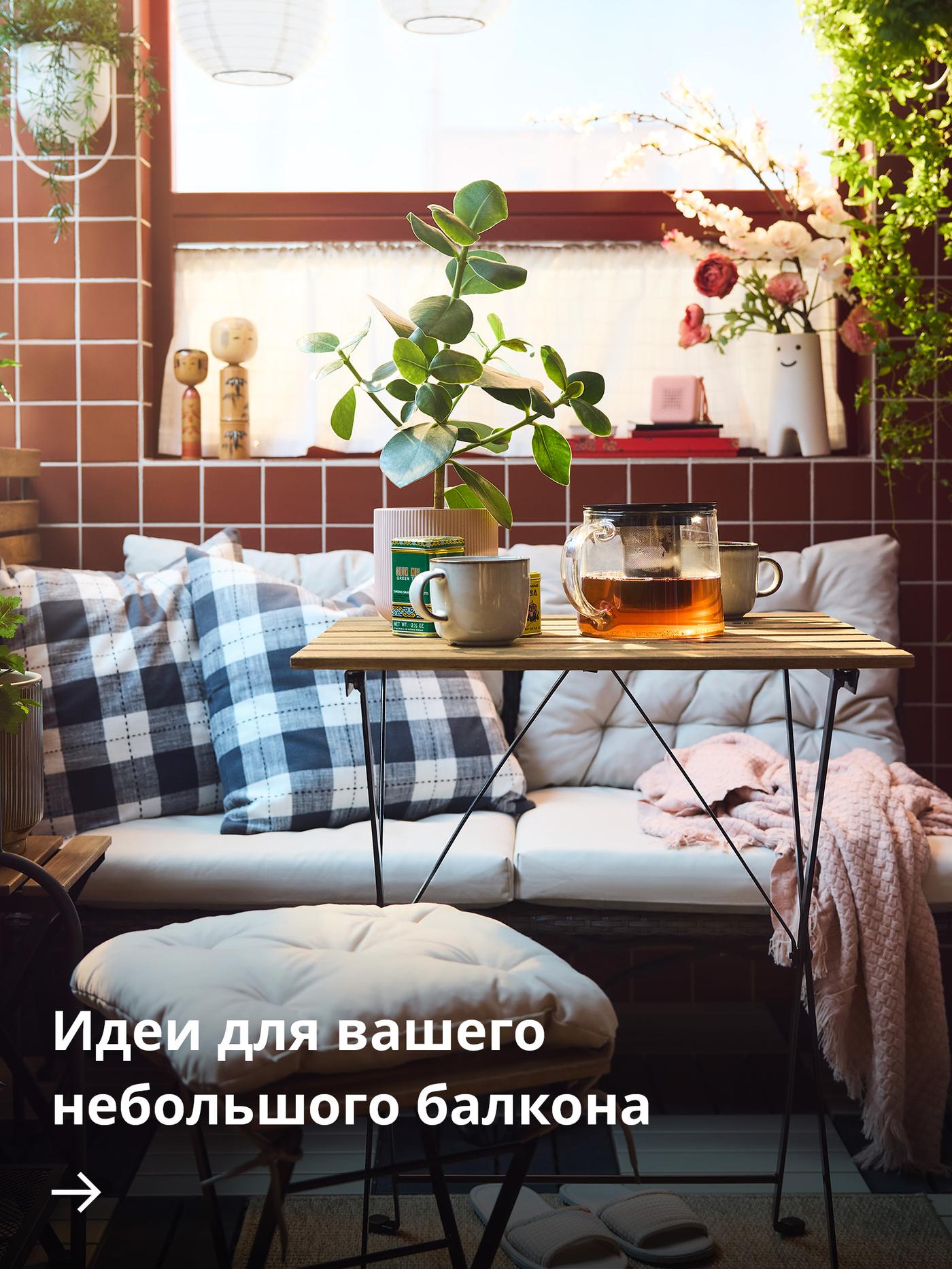 Уютный балкон с красной плиткой, клетчатыми подушками на скамье, небольшим деревянным столиком с кружками и стеклянным чайником, а также растениями в горшках в мягком солнечном свете.