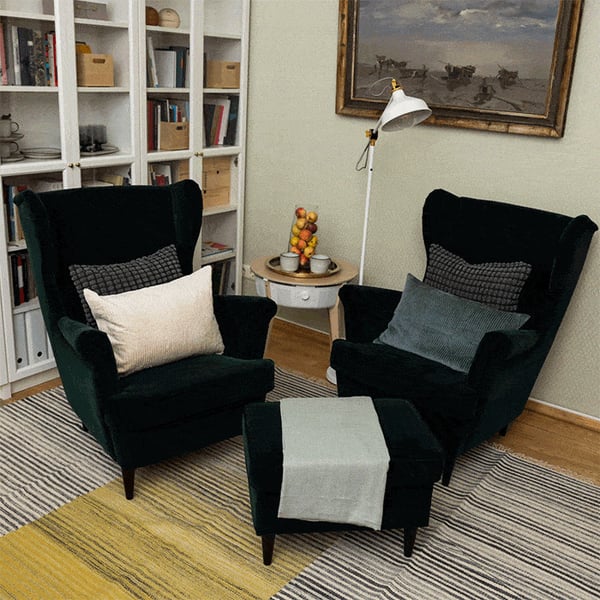 Уютный уголок для чтения с тёмно-зелёными креслами, пуфом, книжным шкафом и торшером