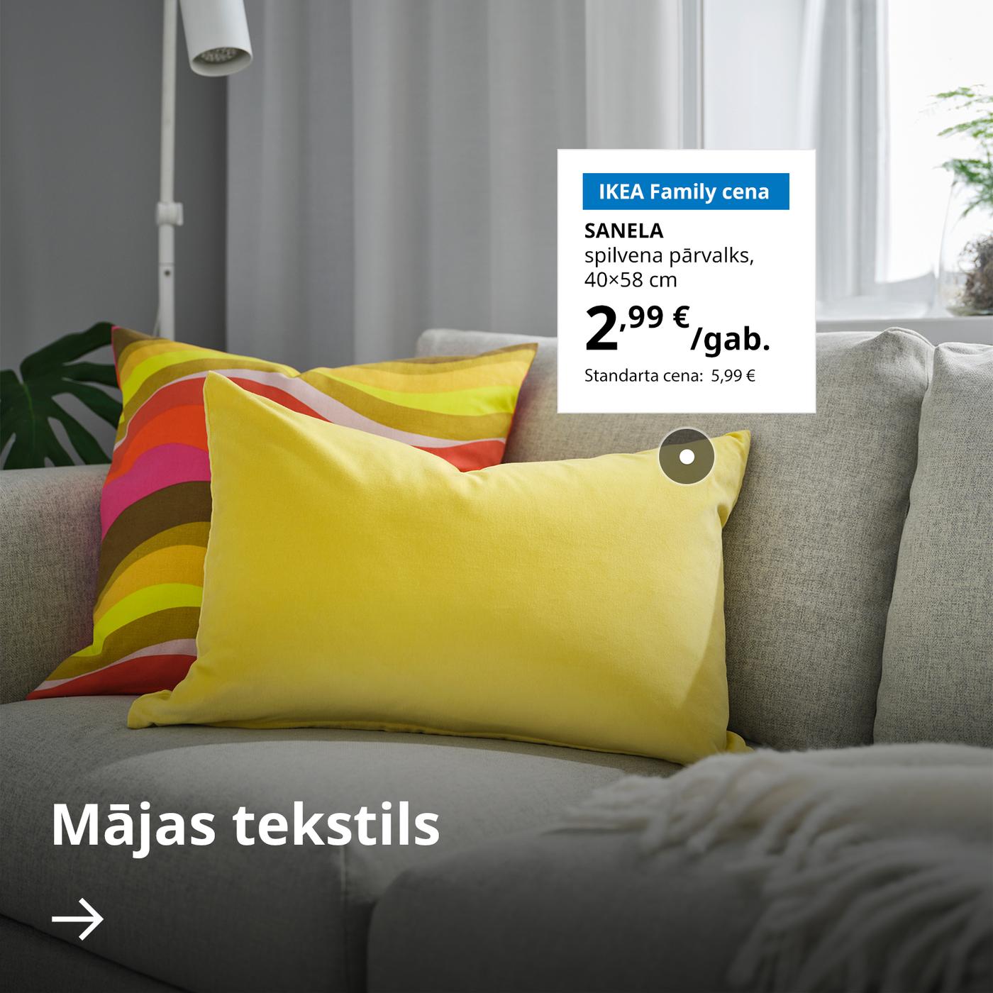 Uz pelēka dīvāna stāv divi spilveni, viens dzeltenā, otrs – daudzkrāsainā pārvalkā. Blakus uz balta fona ir norādīta dzeltenā SANELA pārvalka pazemināta cena – 2,99 € (standarta cena: 5,99 €). Apakšā uzraksts "Mājas tekstils" un zem tā – balta bultiņa.
