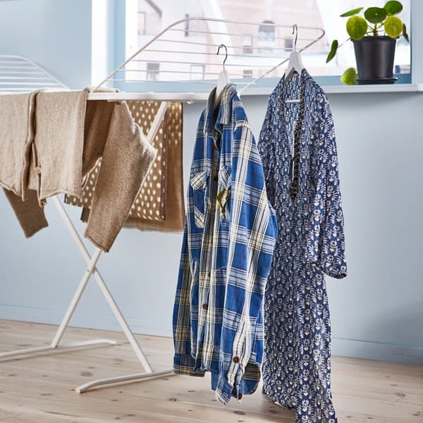 Uz veļas žāvētāja pakarinātas drēbes blakus logam istabā.