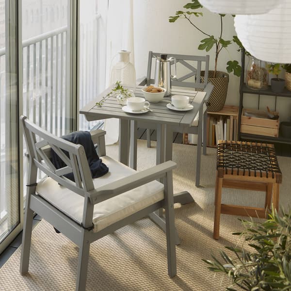 Uzavřený balkon se stolem a dvěma židlemi s opěrkami v šedé barvě, venkovní stolička, bílé závěsné lampy a béžový koberec.