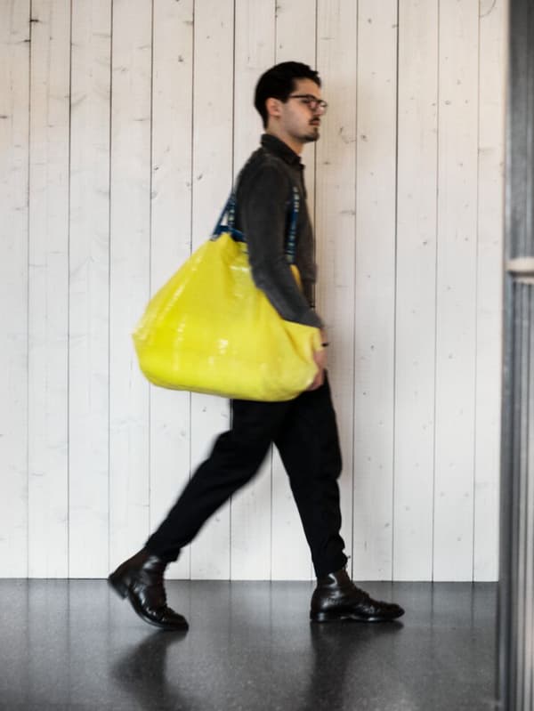 V črno oblečen mladenič hodi po trgovini IKEA in nosi rumeno nakupovalno vrečo.