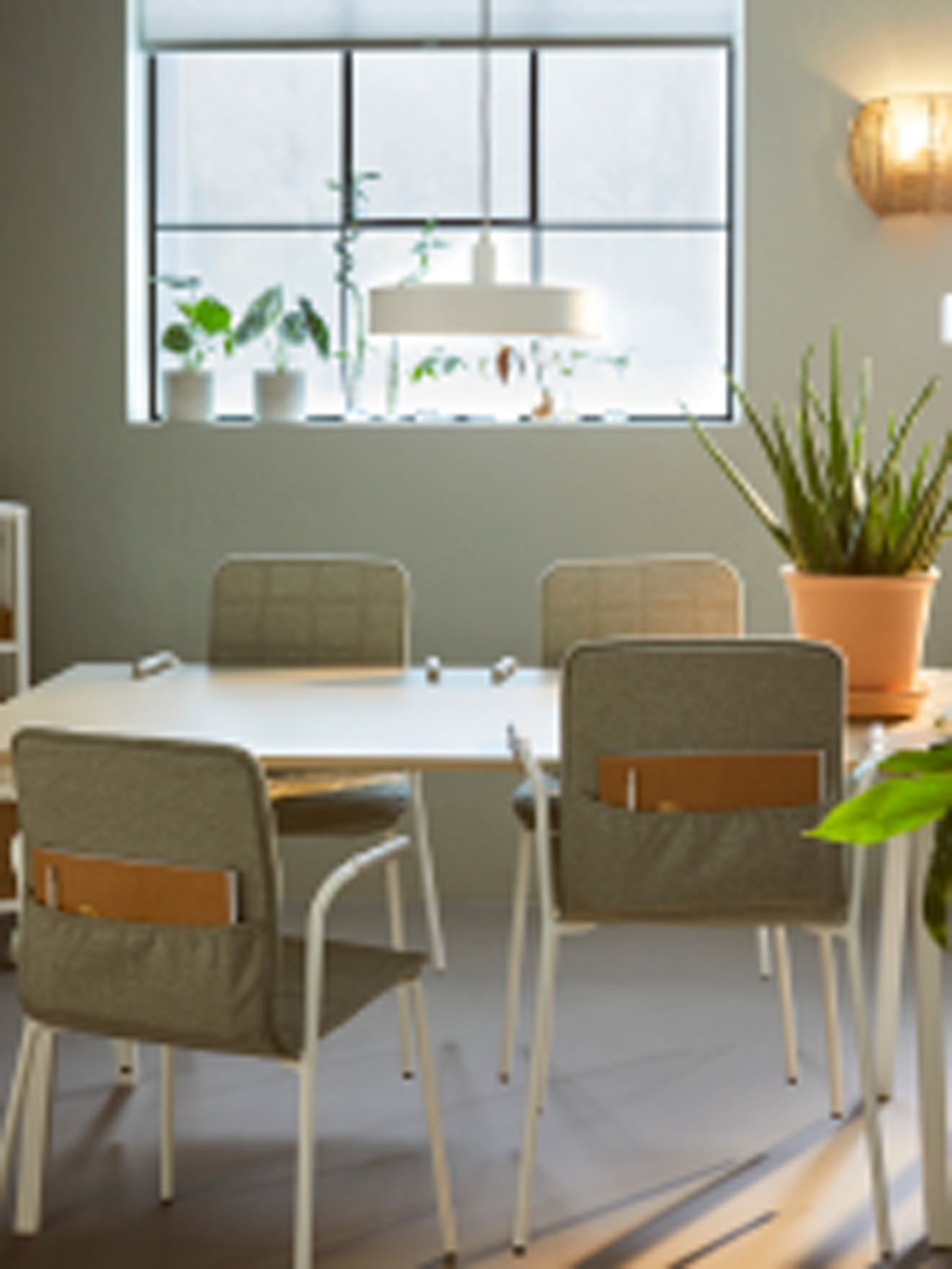 V kancelárskom priestore s oknami v industriálnom štýle sú okolo stola rozmiestnené svetlozeleno-biele konferenčné stoličky LÄKTARE.