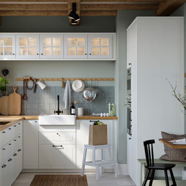 V kuchyni sú biele dvierka a čelá zásuviek a sklené dvierka STENSUND, pracovná doska s dubovým vzorom a biely drez s viditeľným čelom.