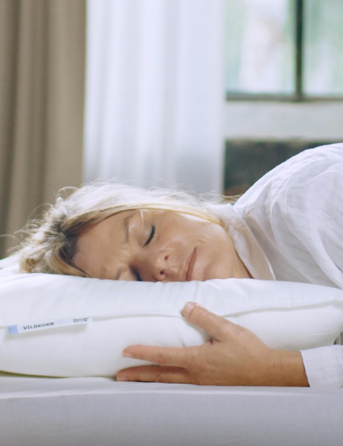 Vaaleahiuksinen henkilö nukkuu vatsallaan matalan VILDKORN-tyynyn kanssa.