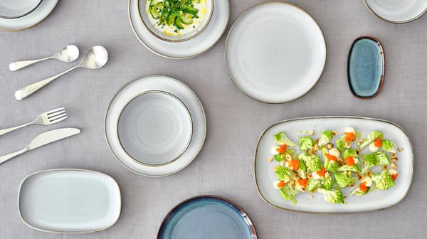 Vaaleita GLADELIG-sarjan astioita on katettu harmaalle pöytäliinalle