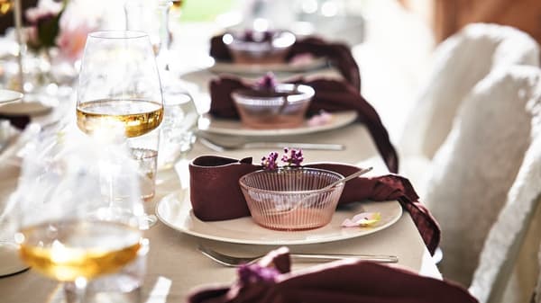 Vackert dukat bord med vinröda servetter, blommor och vinglas.