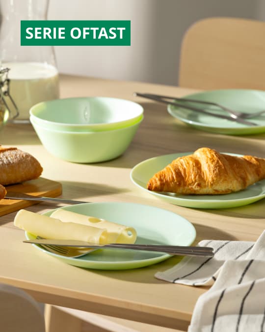 Vajilla verde pastel de la serie OFTASTS sobre una mesa de comedor de madera.