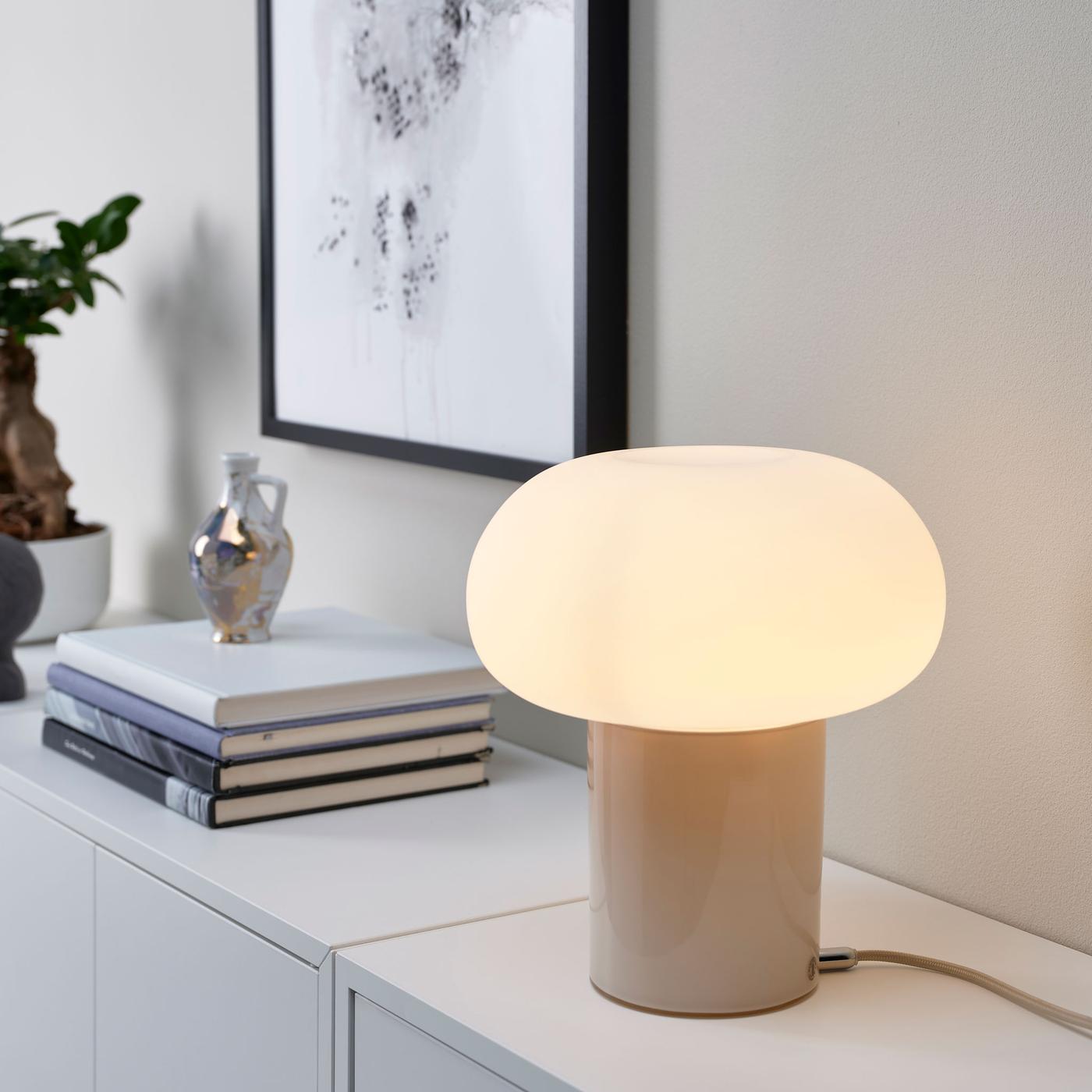 Valkoisella sivupöydällä on DEJSA-pöytävalaisin, kirjoja ja yläpuolella taulu mustilla kehyksillä.