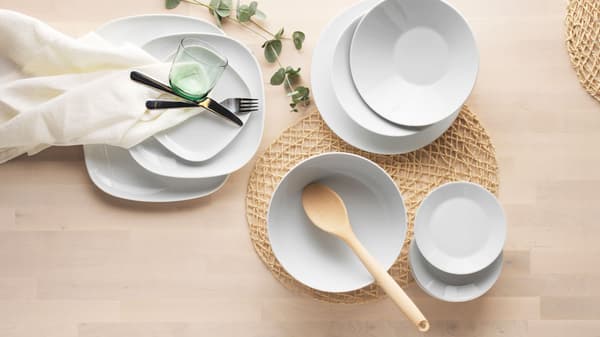 Valkoisia IKEA 365+ -sarjan astioita on pinoissa puisen pöydän päällä.