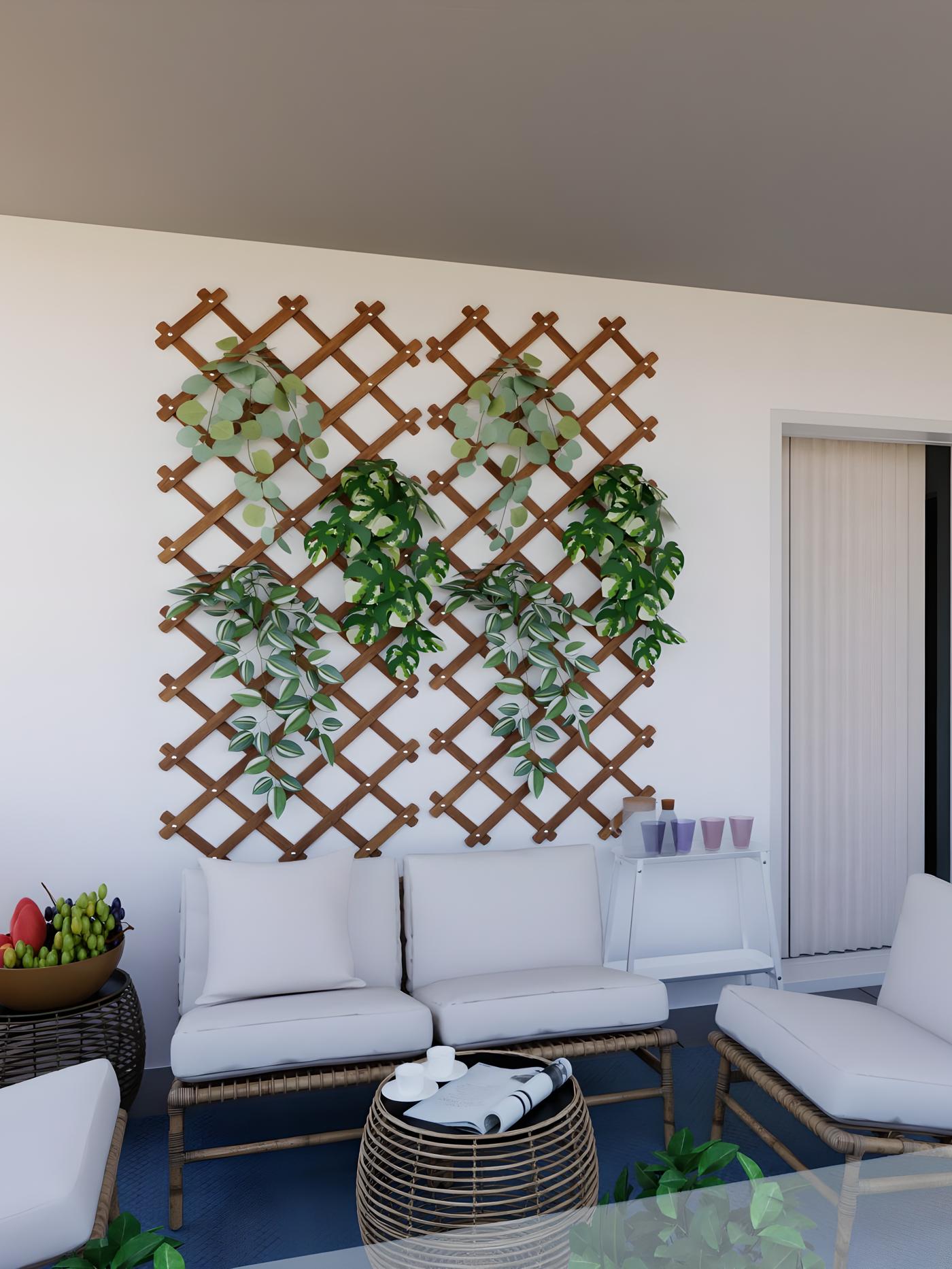 Vanjski prostor s bijelim zidom, drvenim rešetkama i visećim biljkama; garnitura za sjedenje s bijelim jastucima, stolićem i košarom s voćem; desno polica sa šalicama i vrata.