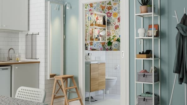Vanuit de keuken leidt een schuifdeur naar een kleurrijke badkamer met bloemetjesbehang en een kleine wastafel.