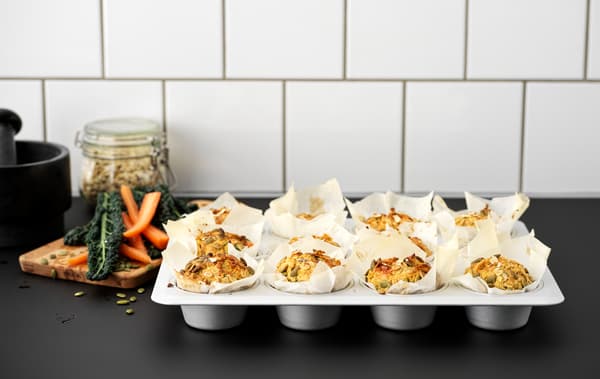 ท็อปครัวสีดำมีถาดอบมัฟฟินทำด้วยเหล็ก VARDAGEN/วาร์ดาเกน ใส่มัฟฟินสิบสองชิ้นซึ่งทำจากแครอทและเมล็ดฟักทอง