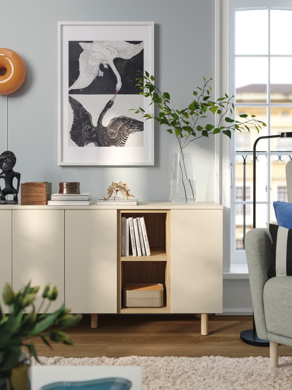 Vardagsrum med en vit byrå, dekorativ konst på väggen, och en grön växt i vas.