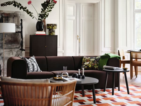 Vardagsrum med mörk soffa, två runda soffbord, blommor i vas och mönstrad matta i rött och vitt.