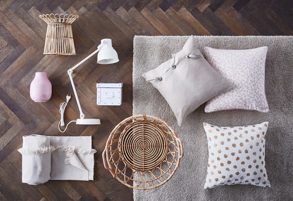 Vari oggetti sul pavimento a creare una moodboard in tonalità crema, pastello e colori neutri. Ci sono cuscini, una lampada da lavoro bianca, un vaso rosa GRADVIS, una scatola, un tessuto e una cesta SNIDAD.