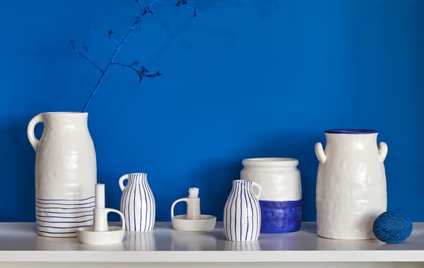 Várias jarras, jarros e castiçais em cerâmica de duas cores, de qualidade rústica e artesanal, colocados em cima de uma mesa de apoio.