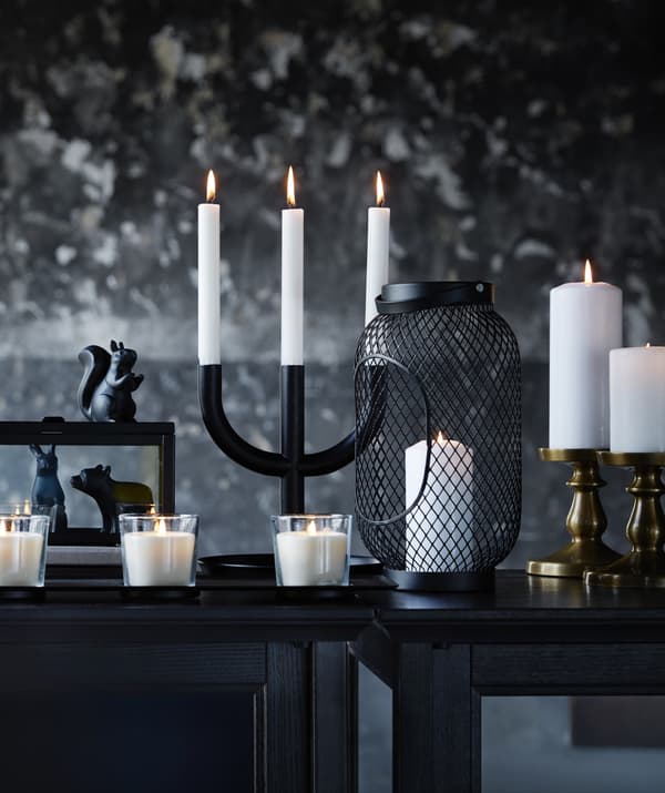 Variété de bougies blanches et de bougeoirs sur une table noire, le tout placé devant un mur marbré noir et gris.