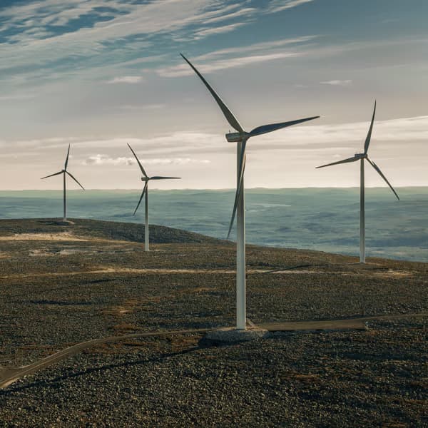 Varios aerogeneradores altos sobre un paisaje montañoso aprovechando la potencia del viento bajo un cielo con nubes.