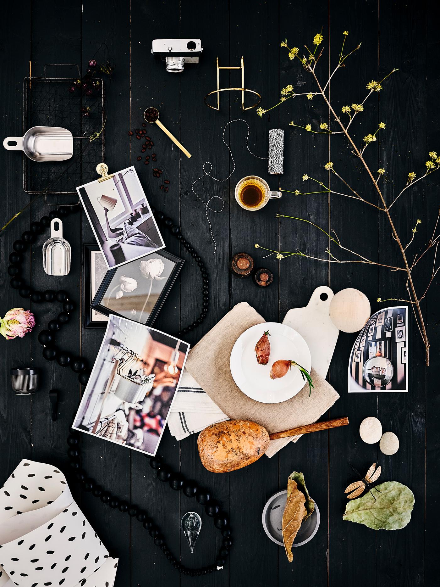 Varios objetos decorativos -un plato blanco OFTAST, tazas medidoras de metal, una ramita en flor- esparcidos por un piso de madera oscura.