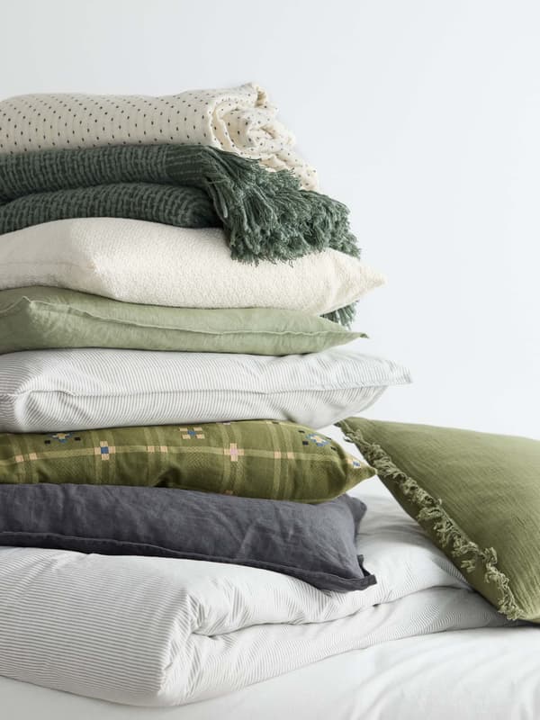 Various bedding in green, cream and gray are stacked on top of each other.