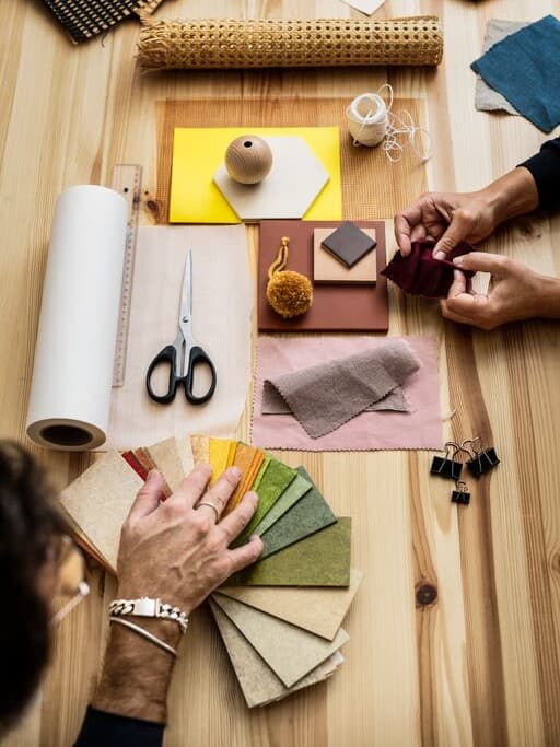 Various fabric samples and colour cards are spread out on a table for room design planning