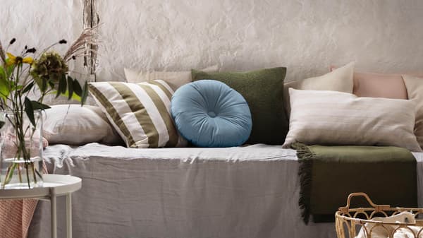 Various throw pillows in green, blue and cream on a bed.