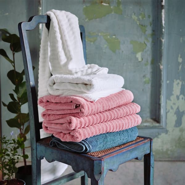 Various towels in gray, pink and white stacked on a dark gray wooden chair, set against a rustic green-gray wooden door.