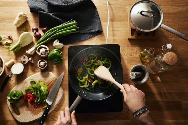 Various vegetables being sauteed in a pan on a TILLREDA portable induction cooktop.