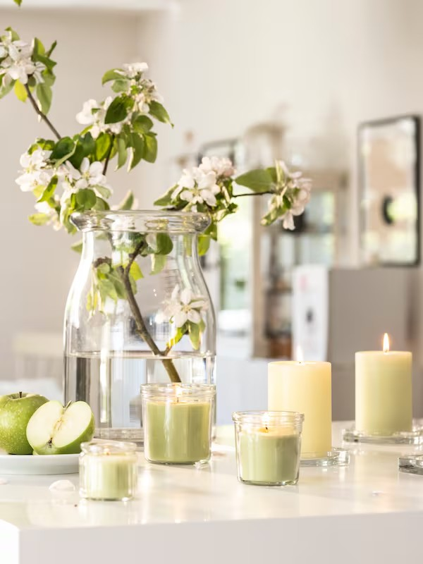 Vase transparent avec des fleurs ainsi que des bougies allumées dans les tons beiges et blancs...