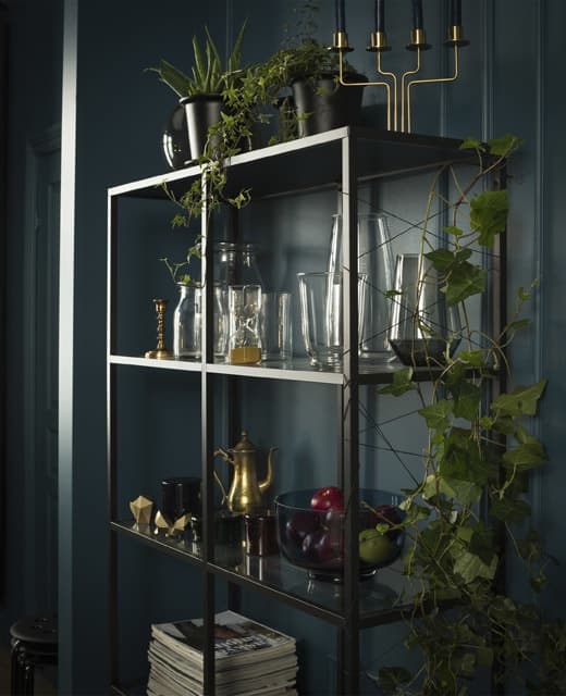 Vasi di vetro e altri oggetti decorativi sono esposti su uno scaffale nero  VITTSJÖ dallo stile essenziale, mentre un traliccio realizzato con lo spago sul lato del mobile sostiene una pianta rampicante.