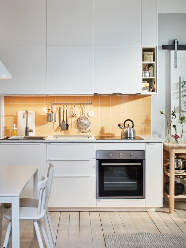 ท็อปครัวพร้อมซิงก์ เตา และเครื่องใช้ในครัว ด้านบนและด้านล่างมีตู้ครัวที่มีบานตู้ VEDDINGE/เวียดดิงเง สีขาวเรียงเป็นแถว