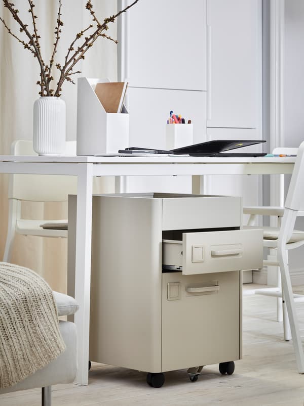 Vedľa postele stojí biely stôl s pracovnými pomôckami a zásuvkovým dielom IDÅSEN pod ním.