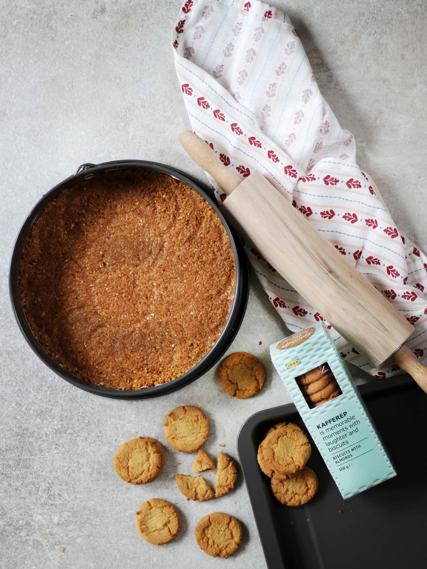 Vedle dortové forma HEMMABAK se sušenkovou směsí leží utěrka INAMARIA, váleček MAGASIN a krabička mandlových sušenek KAFFEREP. 