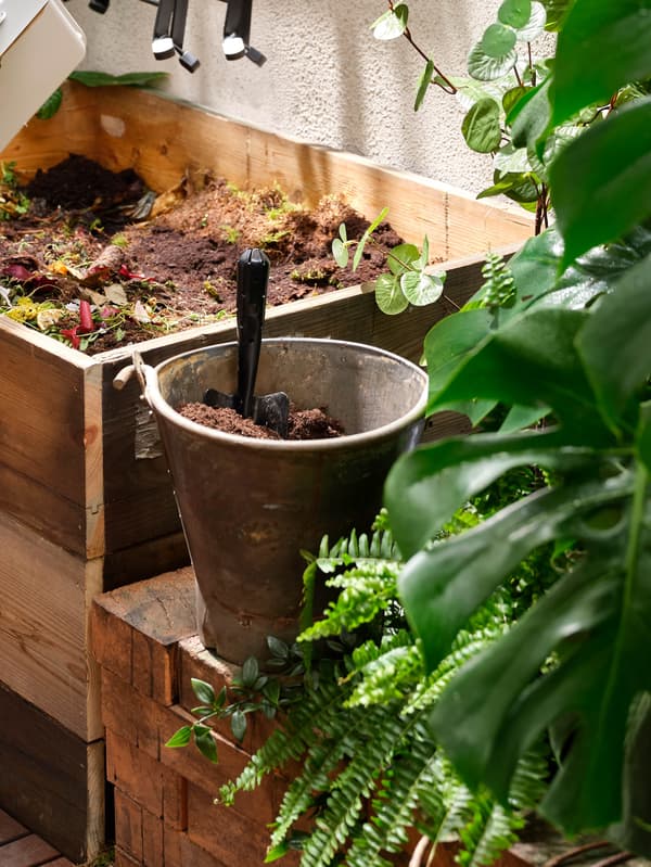 Vedro s lopatkou stojace vedľa kompostéra.