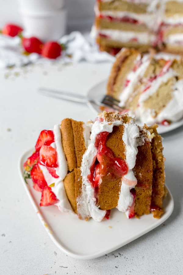 Vegan Strawberry Naked Cake with layers of biscuit, cream and strawberries on white plate 