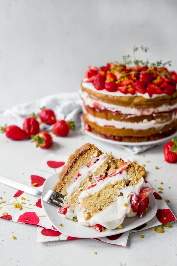 Vegan Strawberry Naked Cake with layers of biscuit, cream and strawberries on white plate and red flower patterned napkin