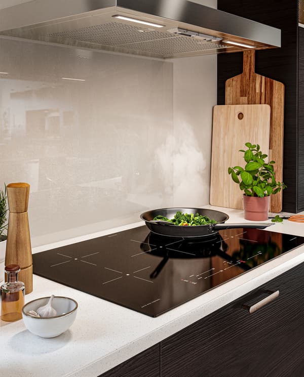 Vegetables are fried in a frying pan that’s placed on a black induction cooktop. Above is a wall-mounted extractor hood.