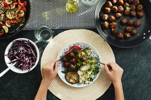 Veggie balls and various greens served on a round, natural coloured, palm leaf SLUTEN place mat.