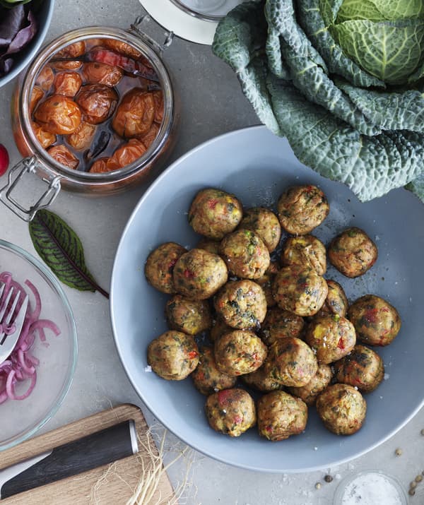 Veggie balls in a blue bowl on a table served with roasted tomatoes in a glass jar and cabbage.