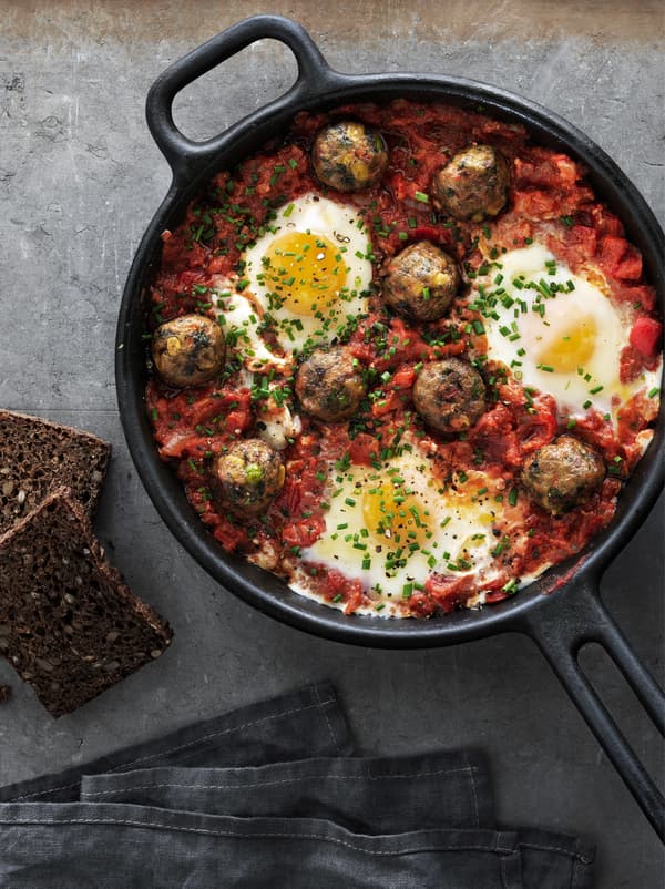 Veggie balls in tomato sauce with poached eggs served in a cast iron frying pan, seen from above.