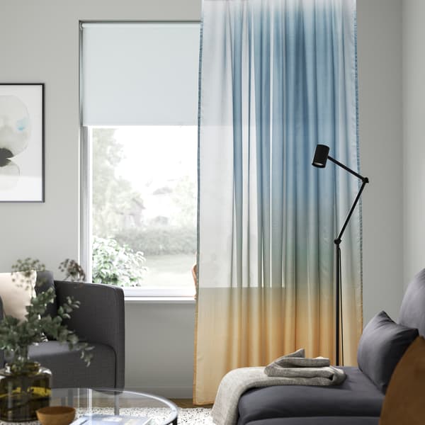 Ventana dentro de un salón con visillo  GLASÖRT compuesto por un degradado de azul a amarillo. 