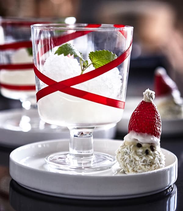 Verre à vin IKEA 365+ décoré d’un ruban rouge et contenant un granité, à côté d’une friandise en forme de bonhomme de neige.