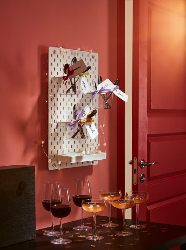 Verre d’accueil servi sur une table basse. Au-dessus, un panneau perforé orné de décorations avec des récipients contenant des cuillères DRAGON, toutes dotées d’un ruban et d’une étiquette nominative.