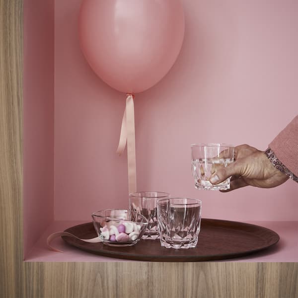 Verres SMAKKÄNSLA et bol en verre VÄLFYLLD posés sur un plateau brun TILLPLATTAD, avec ballon rose.