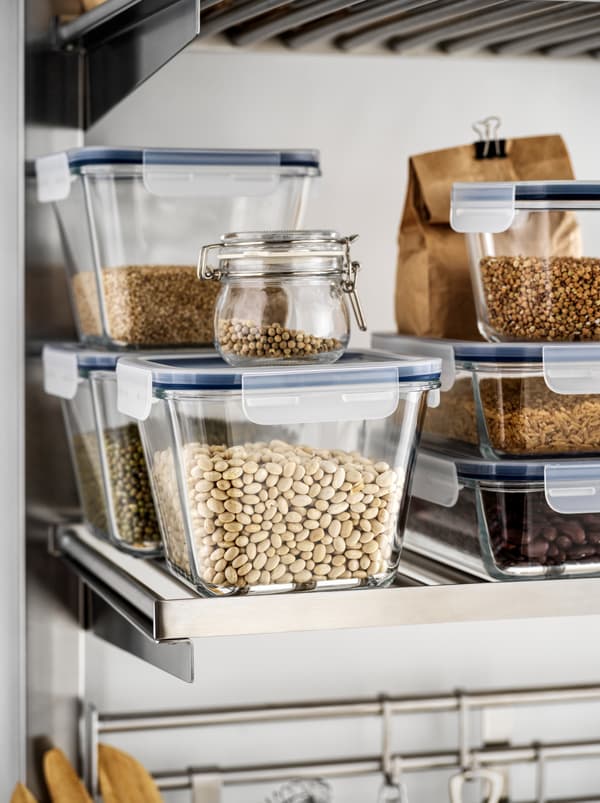 Verschiedene Trockenvorräte – Bohnen, Linsen, Getreide – in IKEA 365+ Glasbehältern auf einem Metallregal in einer Küche.