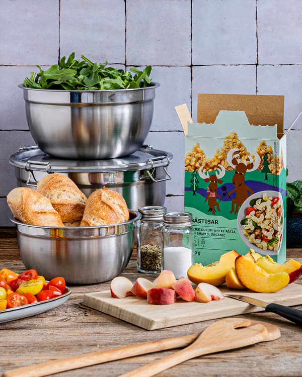 Verschiedene Utensilien für einen sommerlichen Nudelsalat stehen auf einer Küchenablage bereit.