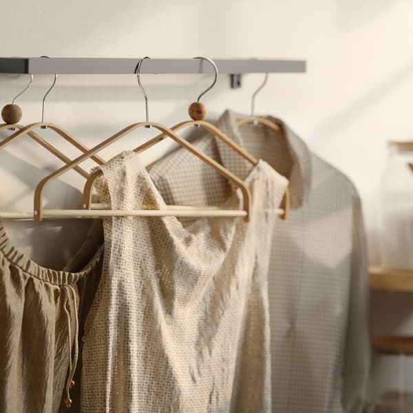 Verschillende bloezen en T-shirts aan HÖSVANS bamboe hangers die aan een metalen wandgemonteerde stang hangen.